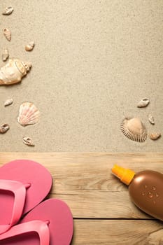 summer concept with pink flip flops,suntan oil and shells on sandy beach. top view