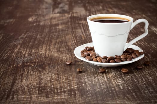 Cup of black coffee with roasted coffee beans on wooden background.
