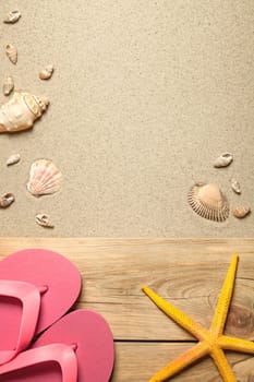 summer concept with pink flip flops,yellow starfish and shells on sandy beach. top view