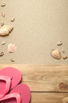 summer concept with pink flip flops and shells on sandy beach. top view