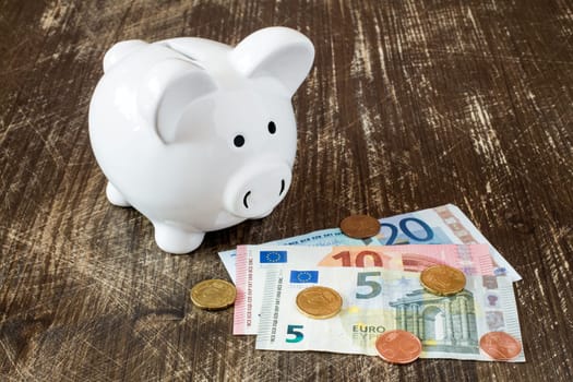 Piggy bank with Euro notes and coins on wooden background