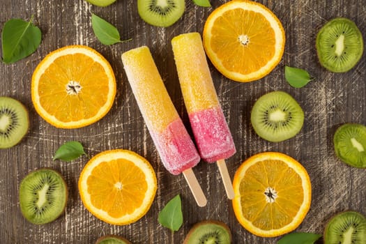 Popsicles with sliced orange and kiwi fruit on wooden background. Top-view.