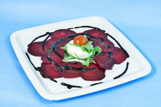 Modern food on a white plate and blue background - Thin slices of beetroot with goat cheese and balsamic reduction