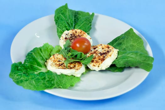 Modern food on a white plate and blue background - grilled goat cheese on roman leaves