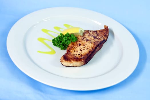 Modern food on a white plate and blue background - grilled salmon with lemon