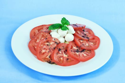 Modern food on a white plate and blue background - tomatoes with mozzarella and basil - caprese salad