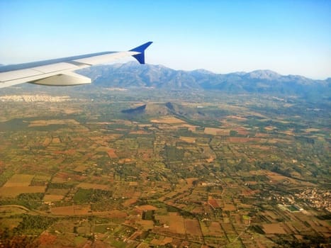 Flight - airplane wing over rural landscape - mountains in background - aerial view from plane during landing approach
