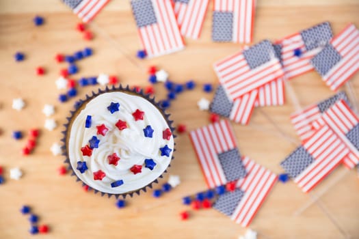 4th of July cupcake with white icing and red and blue stars, viewed from above with flags and stars on table.