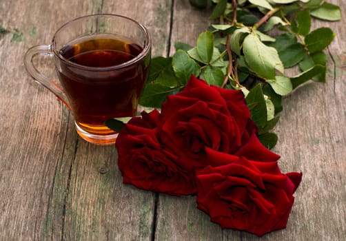 cup of tea and bright red roses on a wooden background, a still life, a subject beautiful flowers and drinks