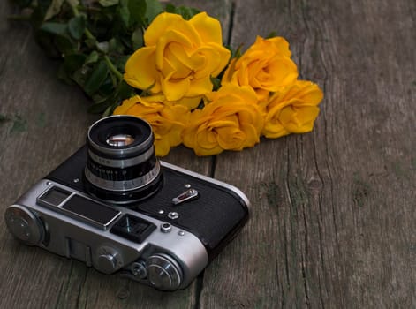 the old film camera and bouquet of yellow roses on a wooden background, a still life, a festive card, a retro the image