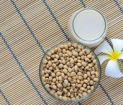 Fresh Soy milk (Soya milk) and dried soybean seeds on bamboo place mat with white plumeria flower. Traditional staple of East Asian cuisine