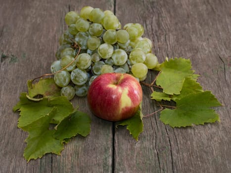 apple and cluster of grapes with leaves on a wooden table, a still life on a subject fruit of fall