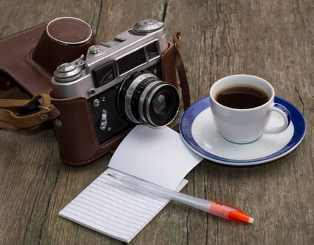 the old camera, coffee and notebook with the handle on a wooden table, a festive card a retro subject