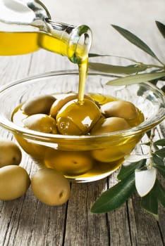 Bottle pouring virgin olive oil in a bowl with green olives close up