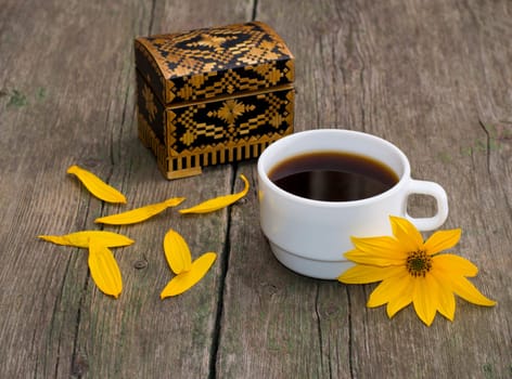 cup of coffee, petals, casket and yellow flower, still life, on a wooden table, a subject flowers and drinks