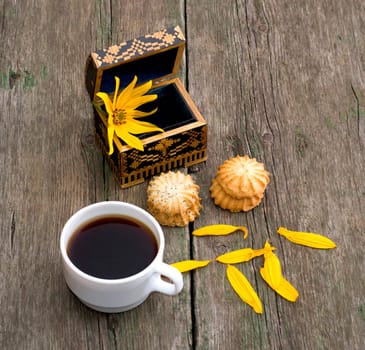 cup of coffee, open casket with a flower, two linking of cookies and petals, a still life on an old table, a subject food and drinks