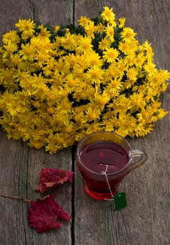 still life, bouquet of yellow flowers, transparent cup of tea and red leaf, on a wooden table, fall, a subject drinks