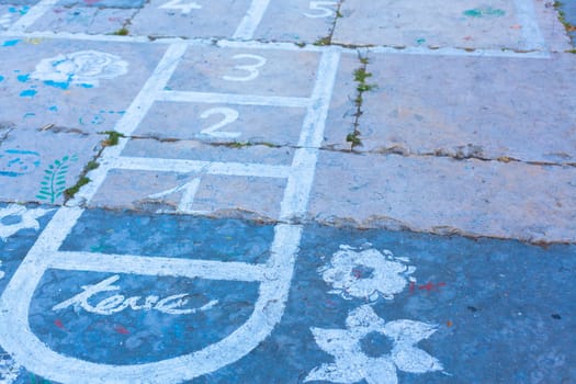 Hopscotch on an asphalt floor with chalk drawings of numbers and squares as an icon of youth innocence and children playing a fun jumping game at recess or after elementary school.