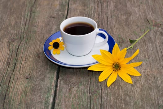 the cup of coffee on a wooden table decorated with two yellow flowers, a still life, a subject fall