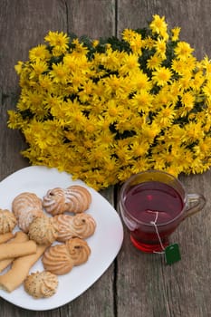 glass of tea, bouquet of yellow flowers and plate with cookies, a still life on a wooden table, a subject food and drinks