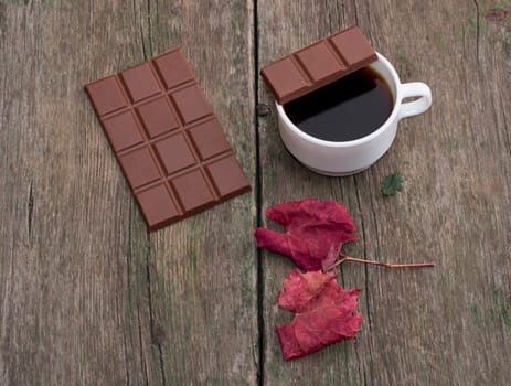 coffee, a piece of chocolate on a cup, nearby chocolate and a red leaf, on a wooden table, the top view, fall, a still life a subject drinks