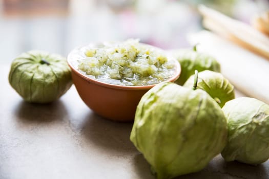Tomatillos and  a bowl of green salsa on stone surface.