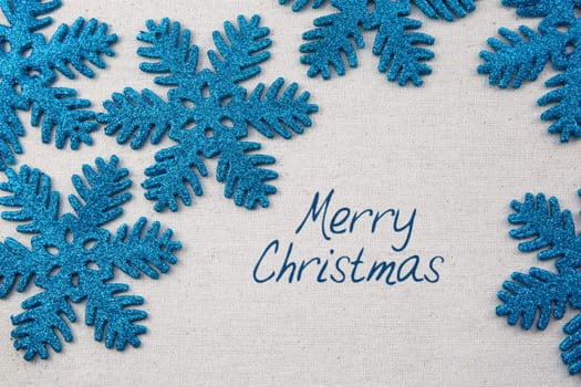 Sparkling blue snowflake ornaments on linen surface with Merry Christmas greeting.