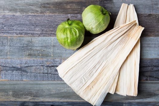 Tomatillos and corn husks on wooden surface with copy space.