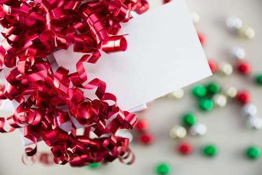 Red curly ribbons on gift box and gift tag with copy space, onaments out of focus in background.