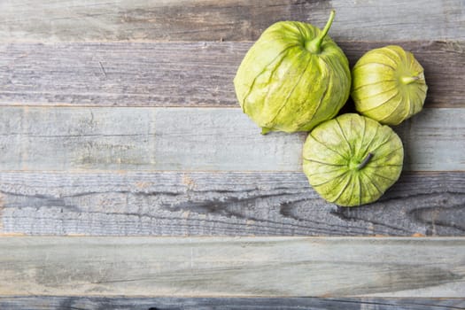 Three tomatillos on wooden surface with copy space.