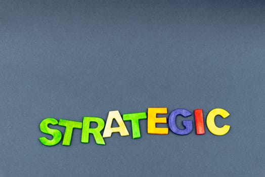 Word STRATEGIC created of wood letters on dark background, business concept, copy space available