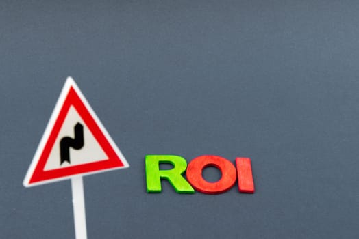 Business Abbreviation ROI as Return On Investment created of wood letters on dark background, Double bend warning road sign and copy space available