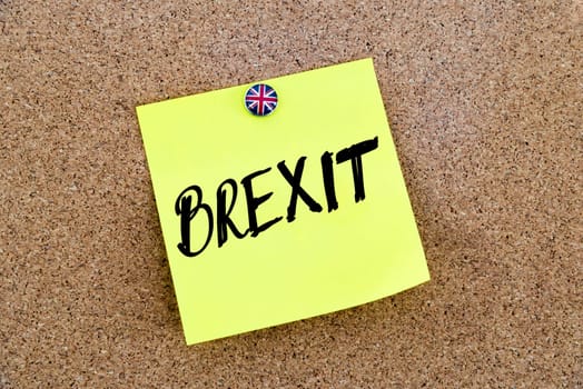 Yellow paper note pinned on cork board with Great Britain flag thumbtack, written text BREXIT, United Kingdom exit from European Union concept