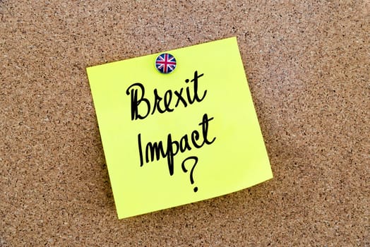 Yellow paper note pinned on cork board with Great Britain flag thumbtack, written text BREXIT IMPACT, United Kingdom exit from European Union concept