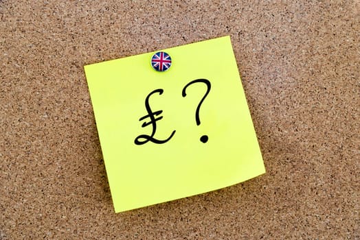 Yellow paper note pinned on cork board with Great Britain flag thumbtack, written Pound Sterling symbol and question mark, United Kingdom exit from European Union concept