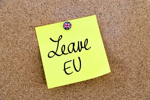 Yellow paper note pinned on cork board with Great Britain flag thumbtack, written text LEAVE EU, United Kingdom exit from European Union