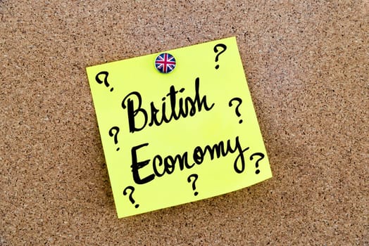 Yellow paper note pinned on cork board with Great Britain flag thumbtack, written text BRITISH ECONOMY and question marks, United Kingdom exit from European Union