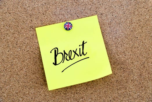Yellow paper note pinned on cork board with Great Britain flag thumbtack, written text BREXIT, United Kingdom exit from European Union concept