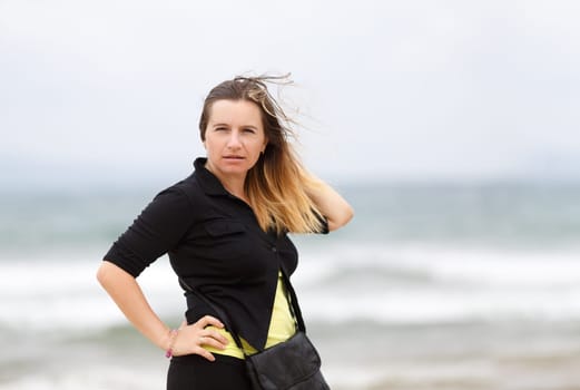 Portrait of a pretty young woman in a black blouse with a blurred background of the sea on a windy day. Shallow depth of field. Focus on the model's face.