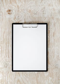 Photo of clipboard with a blank sheet of paper on light wooden background with plenty of copy space. Blank template for design presentations and portfolios. Mock-up for branding identity.
