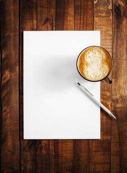 Mock-up for branding identity on vintage wooden table background. Blank letterhead, coffee cup and pen. Mock-up for design presentations and portfolios. Top view.