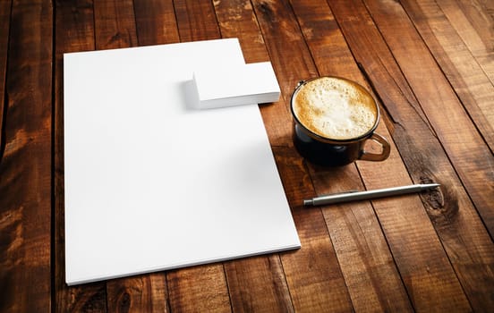 Photo of blank stationery set. Corporate identity template on vintage wooden table background. Letterhead, business cards, coffee cup and pen.