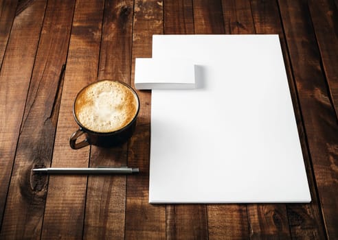 Blank paperwork and corporate identity template on vintage wooden table background. Blank letterhead, business cards, coffee cup and pen. Mock-up for ID. Blank stationery template for design portfolios.