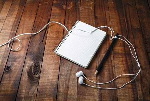 Blank sketchbook with a pencil and headphones on vintage wooden table background. Template for graphic designers portfolios.