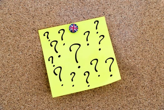 Yellow paper note pinned on cork board with Great Britain flag thumbtack, question marks, United Kingdom exit from European Union