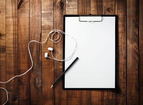 Clipboard with blank white paper, letterhead, pencil and headphones on vintage wooden table background. Mock-up for branding identity for designers. Blank ID template. Top view.