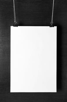 Blank white paper poster hanging on dark background. For design presentations and portfolios. Front view.