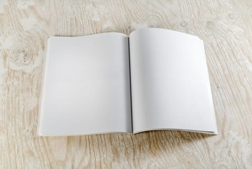 Blank opened book on light wooden background with soft shadows. Mock-up for graphic designers portfolios. Top view.