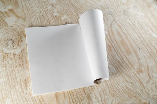Photo of blank opened magazine or album on light wooden background with soft shadows. Template for design presentations and portfolios.