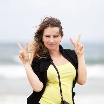 Girl with long hair shows two hands gesture of victory. Selective focus on model.